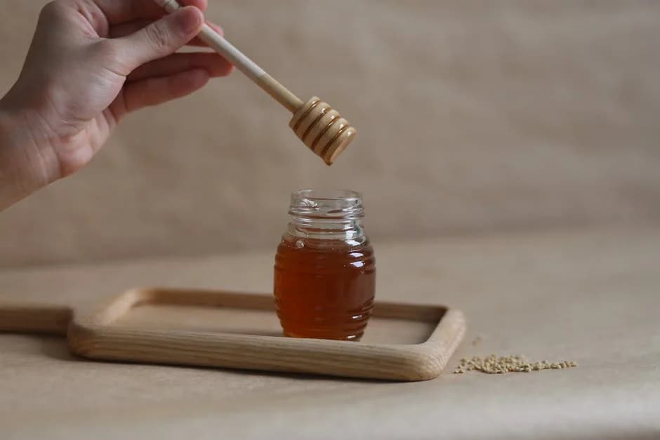 Jar of raw Canaan honey with a wooden dipper, showing its golden amber color and thick texture